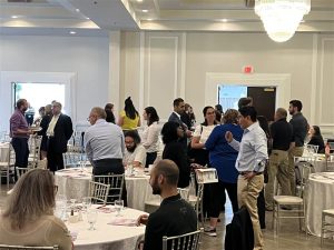 A group of professional looking people networking in an event space, between tables.