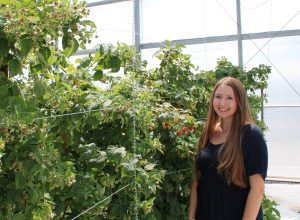 A young woman with long brown hair standing in front of foliage